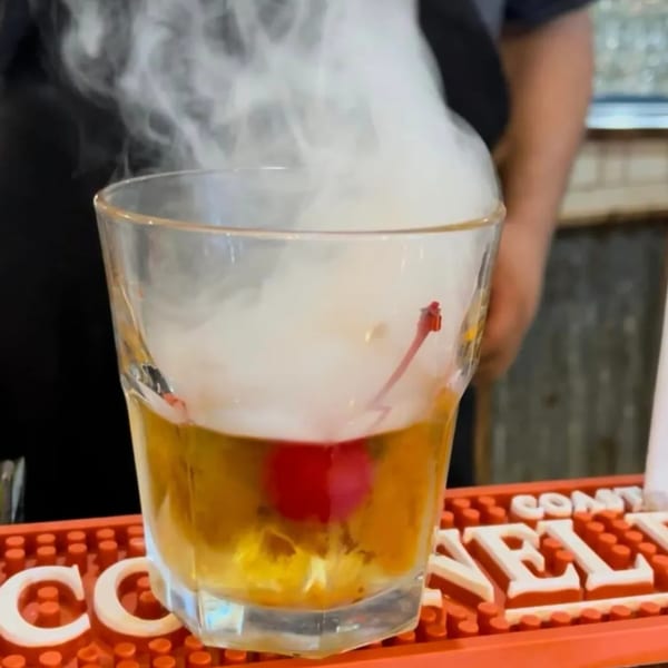 A smoking cocktail with a cherry, served in a glass on a red bar mat at The Original Railroad Seafood Station.