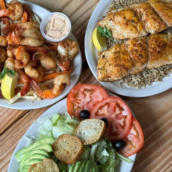 Three plates of seafood dishes: fried shrimp with fries, grilled fish with rice, and a fresh salad.