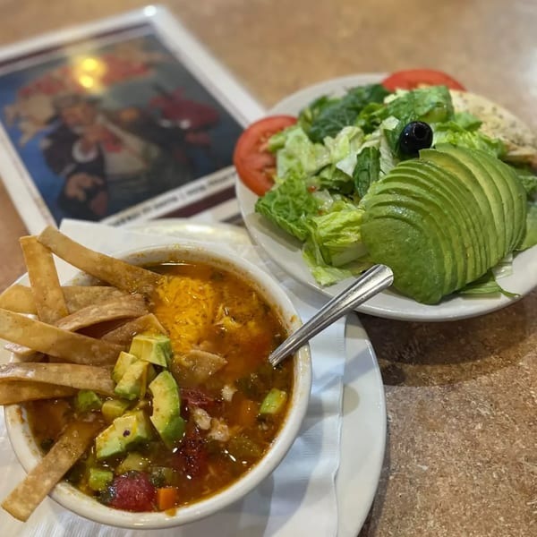 Seafood soup with tortilla strips and avocado, alongside a fresh salad with sliced avocado.