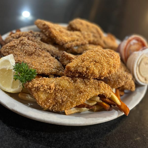 A plate of golden-brown fried seafood and french fries, garnished with a lemon wedge and parsley.