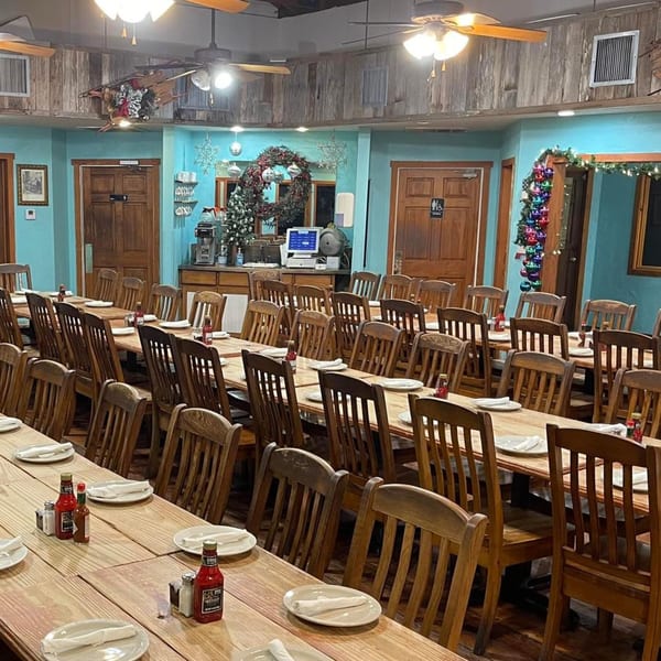 Long wooden tables with chairs, set with plates and condiments, in a dining room with blue walls.