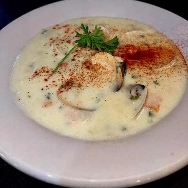 Creamy seafood chowder with clams, mussels, paprika, and a parsley garnish in a white bowl.