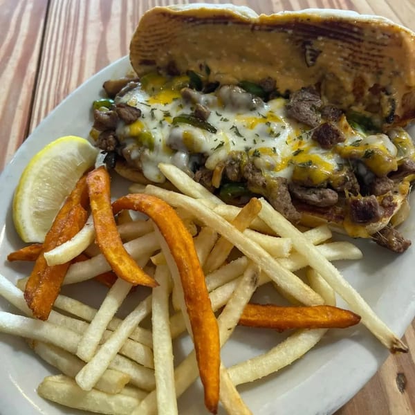 A cheesesteak sandwich with peppers and onions, served with a side of french fries and sweet potato fries.