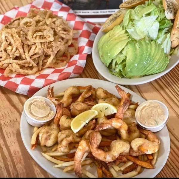 Fried shrimp and fries with lemon, a side salad, and a basket of onion strings.
