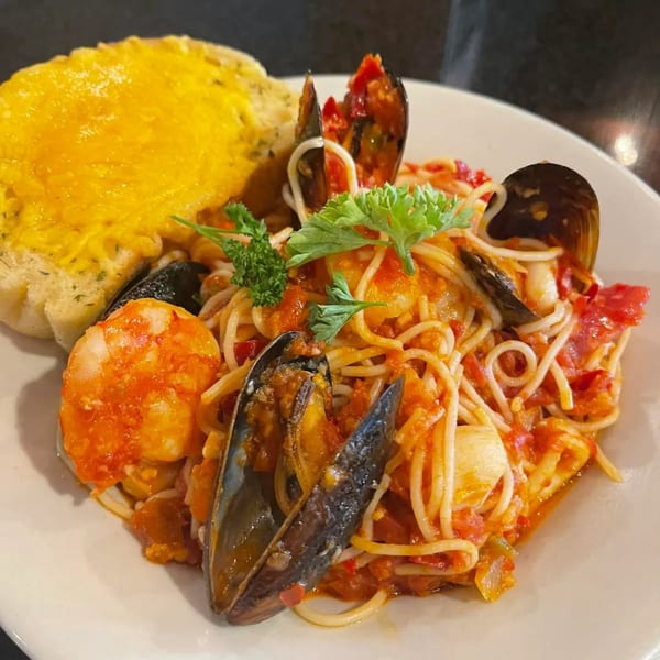 Seafood pasta with mussels, shrimp, and red sauce, garnished with parsley and a side of cheesy bread.