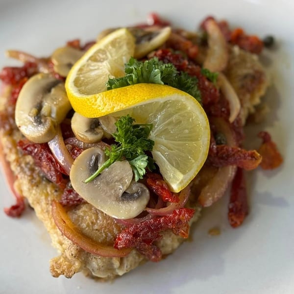 Seafood dish topped with mushrooms, red onions, sun-dried tomatoes, parsley, and lemon slices.