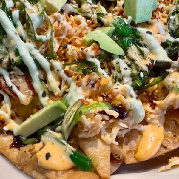 Close-up of seafood nachos with white and orange sauces, green onions, and avocado slices.