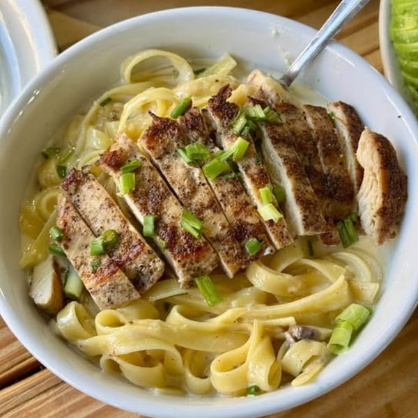 Blackened chicken fettuccine alfredo, topped with green onions, served in a white bowl.
