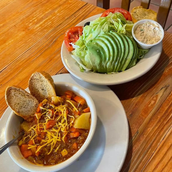 Hearty chili with shredded cheese and bread, alongside a fresh salad with avocado and tomatoes.