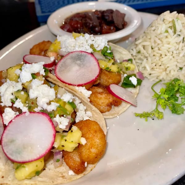 Two shrimp tacos with pineapple salsa, radishes, and feta cheese, served with rice and beans.